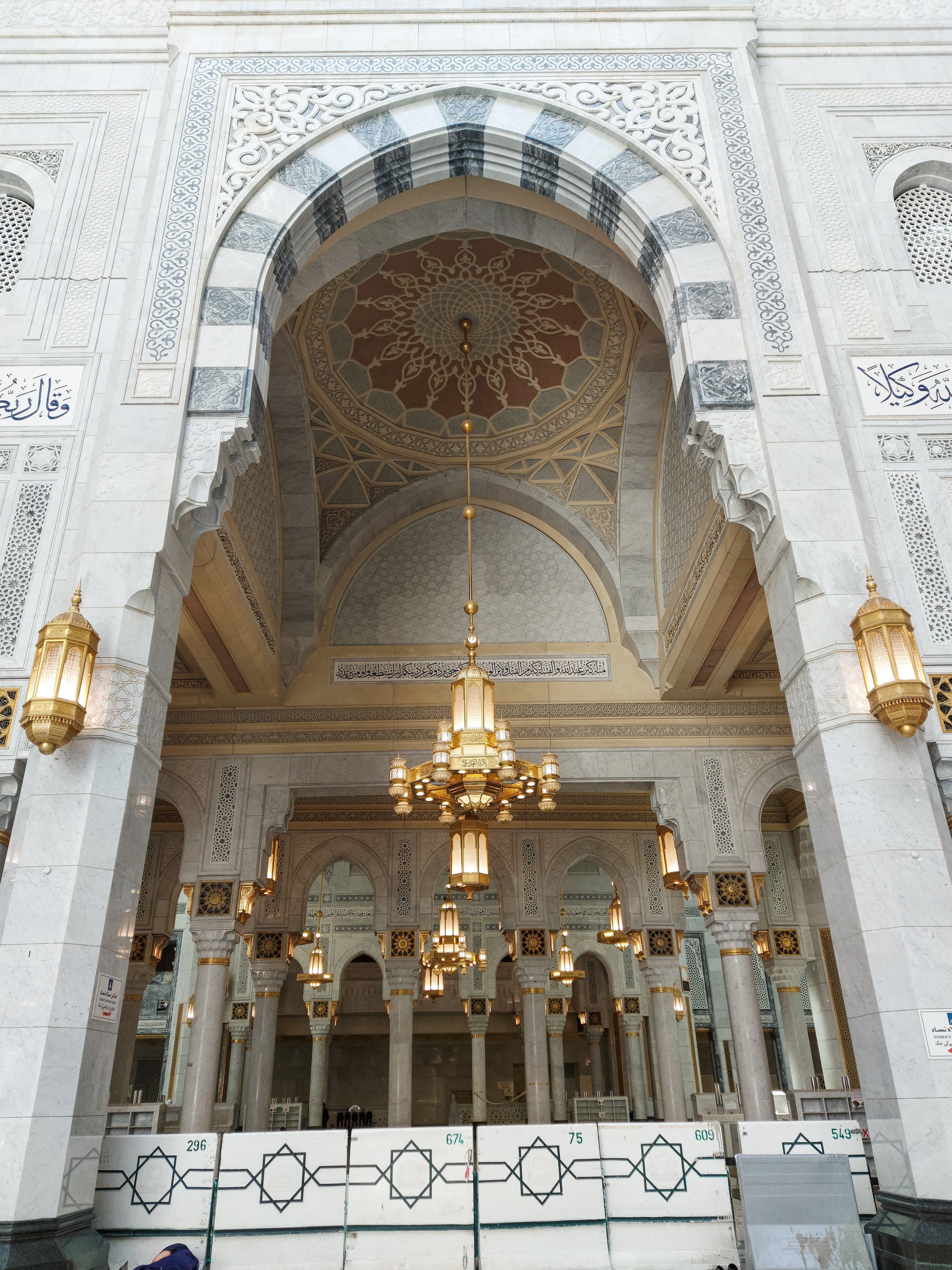 Detail view of the Holy Mosque in Makkah showing golden Arabic calligraphy and ornate crystal lamps