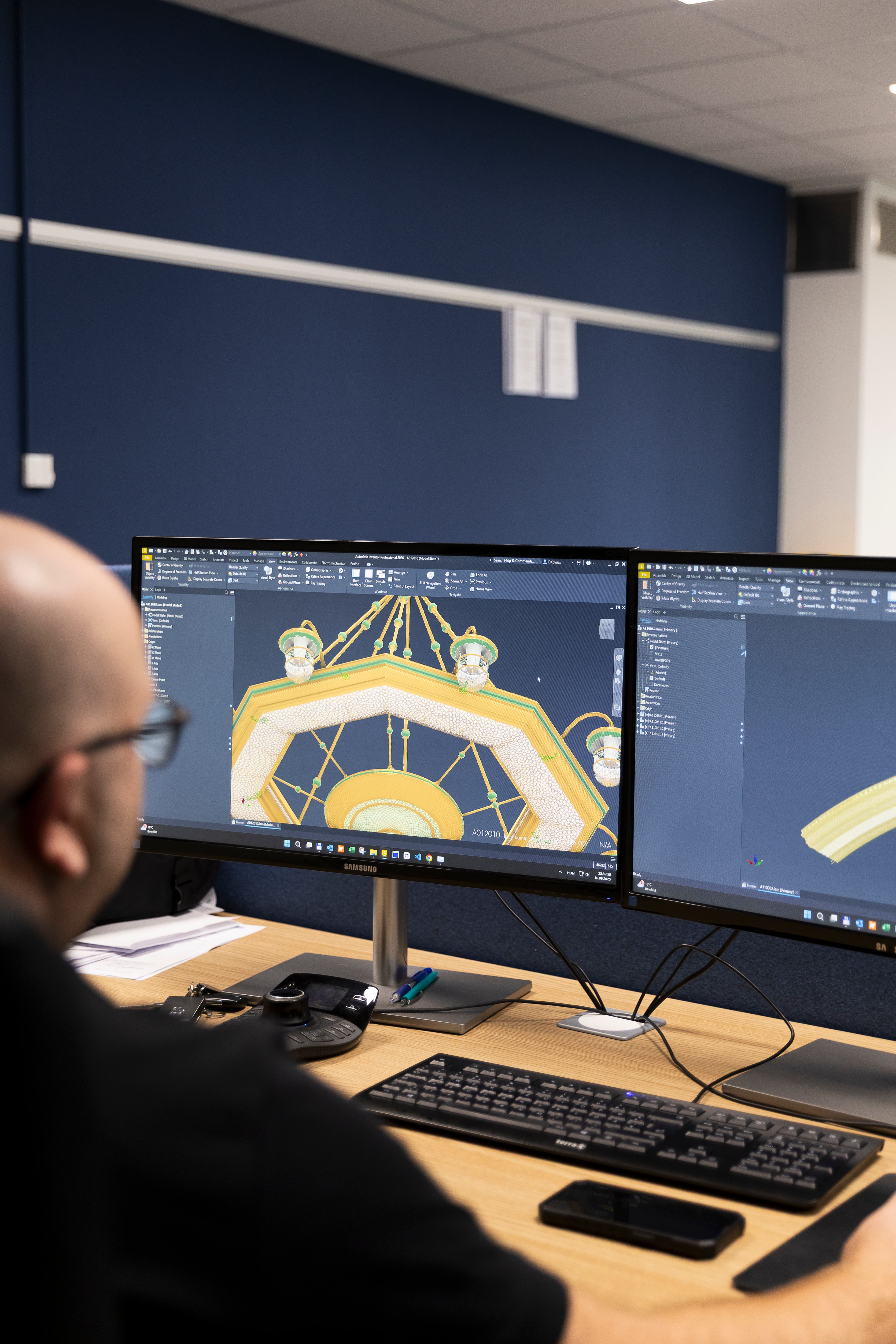 Technican wearing a "Lights of Vienna" shirt, working on a large circular golden chandelier with intricate mesh details in a workshop setting