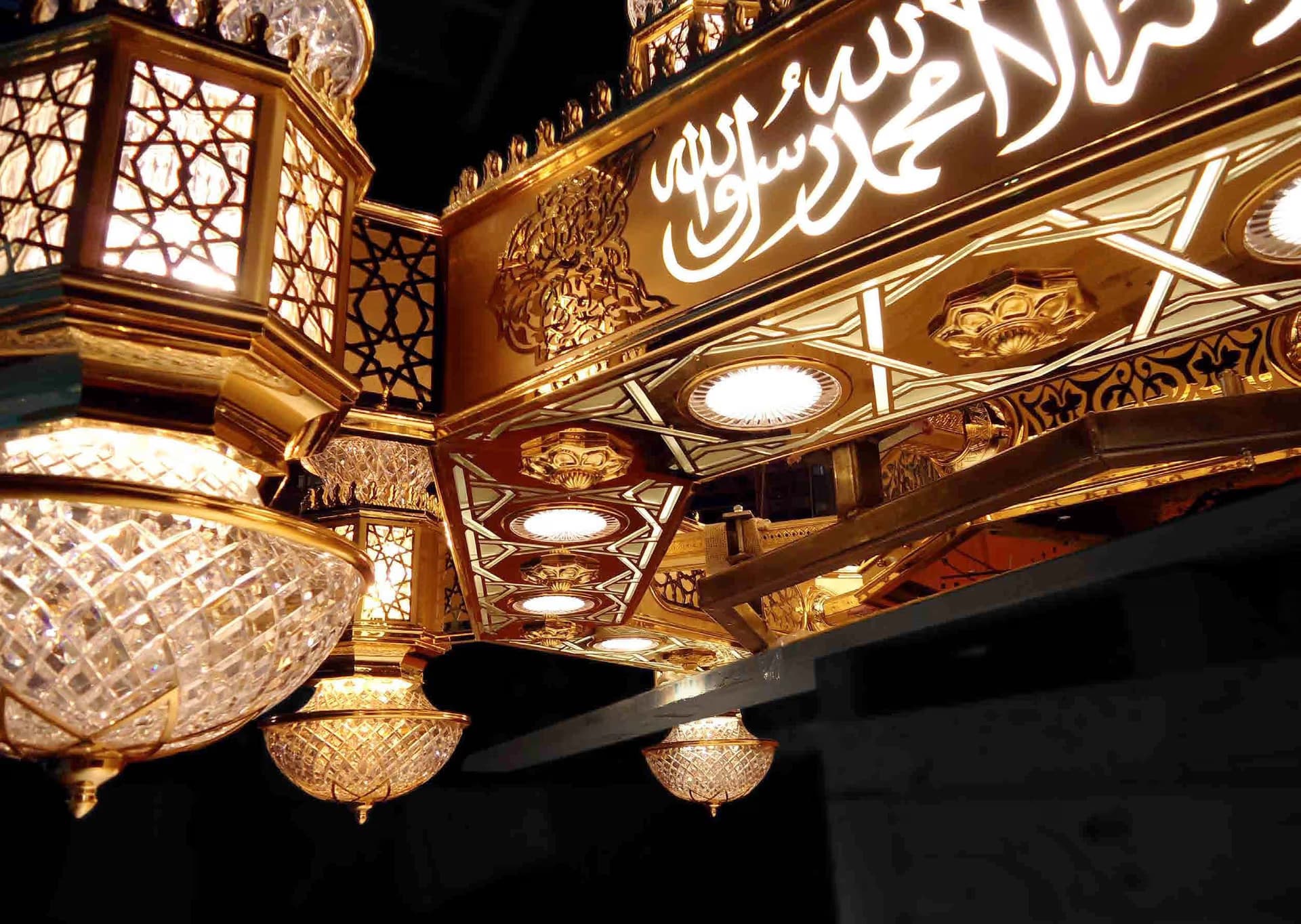 Detail view of the Holy Mosque in Makkah showing golden Arabic calligraphy and ornate crystal lamps