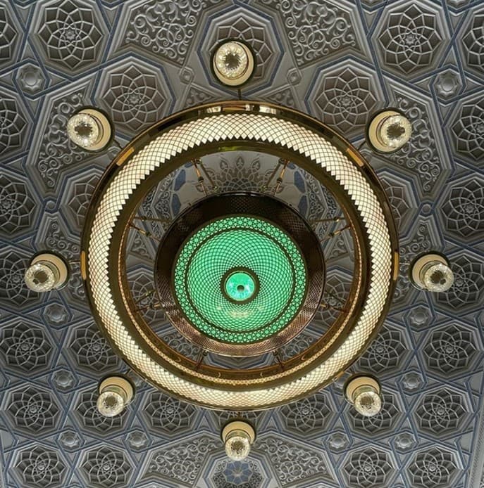 Ceiling light detail of the Holy Mosque in Makkah featuring a golden chandelier with green glass and intricate geometric patterns